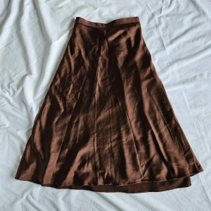 Brun satin kjol - strl. 36 - En silkeslen midikjol med dragkedja och knapp på sidan. Bra skick!