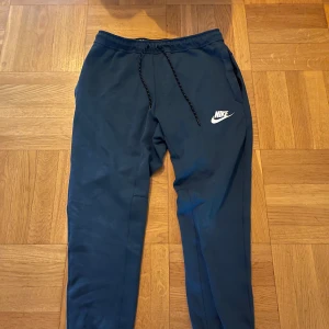 Svarta mjukisbyxor från Nike - Säljer ett par svarta mjukisbyxor från Nike med snörning i midjan och det klassiska Nike-loggan på benet. Perfekta för en avslappnad stil.
