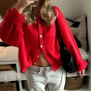 Röd kofta med knappar - Snygg röd kofta med knappar framtill. Den har en lös passform och långa ärmar, perfekt för en avslappnad stil. Koftan är tillverkad i ett mjukt material som ger en skön känsla.