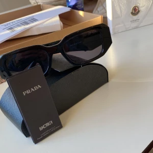 Svarta solglasögon från Prada - Snygga svarta solglasögon från Prada med en rektangulär form. Glasögonen har en elegant och stilren design. Perfekta för en trendig look.