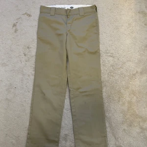 Beige byxor från Dickies - Snygga beige byxor från Dickies med rak passform. Perfekta för en avslappnad stil. Byxorna har hällor för bälte och en klassisk design med två bakfickor.