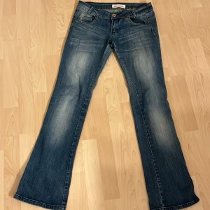 Blå bootcut jeans från Revan Jeans - Snygga lågmidjade blå bootcut jeans från Revan Jeans med slitna detaljer. ( Gylfen var trasig men är lagad )