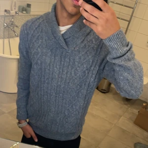 Grå stickad tröja med krage - Säljer en stilren grå stickad tröja från Bergman med en snygg krage. Tröjan har ett klassiskt flätmönster och långa ärmar. Pris kan diskuteras 
