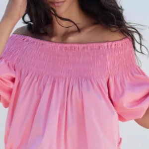 Rosa offshoulder topp - Söt rosa offshoulder topp med smockdetaljer vid halsen. Toppen har korta puffärmar och en luftig passform, perfekt för varma sommardagar.