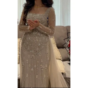 Champagnefärgad klänning med pärlor - Elegant champagnefärgad långklänning med långa ärmar och detaljerade pärlor. Klänningen har en korsett så den passar storlekarna 34-38.                            • Avtagbar kjol.                                                                   • Enbart använd 1 gång på min förlovning.                                                    • Pris kan diskuteras vid snabb affär.