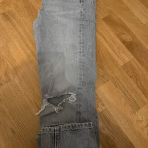 Grå jeans från Zara - Snygga grå jeans från Zara med slitna detaljer och en klassisk femficksdesign. De har en dragkedja och knapp framtill. Perfekta för en avslappnad look.