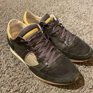 Philippe Model trainers TRPX - Snygga svarta sneakers från Philippe Model med gula detaljer och snörning. Skorna har en unik design med en kontrasterande vit detalj på sidan och en bekväm sula. Rejäla och tåliga skor med bra kvalitet, funkar fint som vintersko. Mycket bra skick. Nypris 3211kr, säljes för 750.
