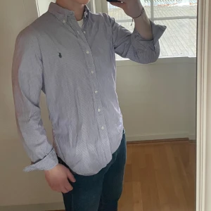 Vit och Lila randig Ralph lauren skjorta - Randig skjorta från Ralph Lauren. Vit och lila ränder, men ser i princip som blått och vitt. Storlek: L, slim fit. Skick: 9/10, väldigt fint skick, skjortan är bara lite ostruken. Nypris: 2300kr. Kontakta oss för fler bilder eller info!🙌