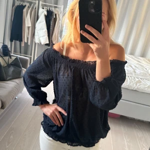 Marinblå offshoulder blus från Mango - Säljer en elegant marinblå offshoulder blus från Mango. Blusen har ett prickigt mönster och långa ärmar med elastiska muddar. Perfekt för en stilren look. Man kan ha den både off shoulder och vanligt då den är stretchig. Hör av dig vid intresse!