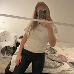 Vit kortärmad topp med rynkdetaljer - Säljer en stilren vit kortärmad topp med rynkdetaljer i midjan. Perfekt för en avslappnad men ändå chic look. Passar bra till både jeans och kjol.