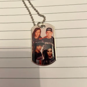 Halsband med bandmotiv - Coolt halsband med en bricka som har ett tryck av ett band. Kedjan är av kulmodell och brickan har en rektangulär form med rundade hörn. Perfekt för musikälskare som vill visa sin stil.