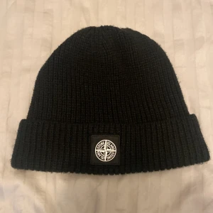 Svart mössa från Stone Island - Jag säljer en stilren mössa från Stone!! Materialet är mjukt och bekvämt, den håller dig varm och kliar inte. Den är använd 2-3 gånger utan några defekter!! Nypris≈1700. Jag kn mötas i Stockholm och posta överallt. 