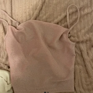 Glittrig rosa topp - Säljer en glittrig rosa topp med smala axelband. Perfekt för en festlig kväll eller en somrig dag. Toppen har en enkel och stilren design som gör den lätt att matcha med olika outfits.