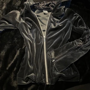 Svart velourjacka från Nike - Säljer en snygg svart velourjacka/tracksuit jacka från Nike med dragkedja framtill. Den köptes i Paris. Jackan har en sportig look med långa ärmar och en liten Nike-logga på bröstet. 