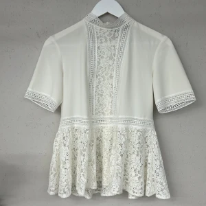 Vit spetsblus från Zara - Elegant vit blus från Zara med vackra spetsdetaljer och korta ärmar. Blusen har en fin volangkant och en diskret dragkedja i ryggen. Perfekt för en stilren look.