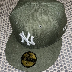 Grön keps från New Era - Snygg grön keps från New Era med klassisk logga framtill. Kepsen har en rak skärm och är tillverkad i polyester. Perfekt för att ge din outfit en sportig touch.