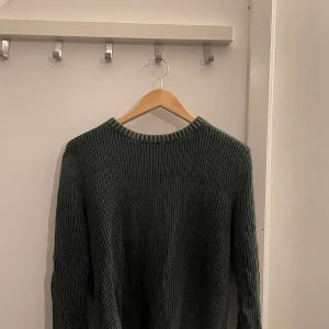 Grön stickad tröja - Säljer en stilren grön stickad tröja från Lagency. Perfekt för kyligare dagar med sin mjuka och bekväma passform. Tröjan har långa ärmar och en klassisk design som passar till det mesta. 