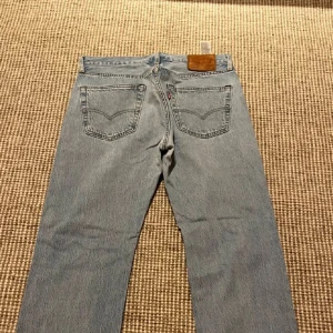 Blå jeansbyxor från Levi's - Snygga blå jeansbyxor från Levi's med klassisk femficksdesign och en rak passform. Byxorna har en läderpatch med logotyp baktill och en ikonisk röd etikett på bakfickan. Perfekta för en avslappnad stil.