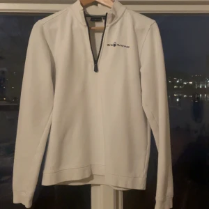 Vit tröja från Sail Racing - Säljer en stilren vit tröja från Sail Racing med dragkedja vid halsen. Tröjan har långa ärmar och en liten logotyp på bröstet. Perfekt för en avslappnad och sportig look. Ny pris 800