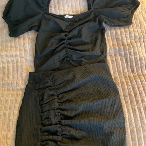 Svart klänning med puffärmar - Snyggt svart sätt med puffiga kortärmar och rynkade detaljer framtill. Perfekt för en stilren look med en touch av elegans.  har en smickrande passform och är gjord i ett lätt material.