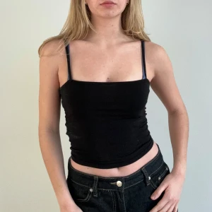 Svart linnetopp - Snygg svart ärmlös linnetopp med smala axelband. Perfekt för en stilren och enkel look. Passar bra till både jeans och kjol. Väldigt skönt material! 