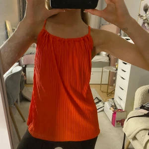 Orange topp - Säljer en snygg orange topp med tunna axelband och öppen rygg. Den är aldrig använd och har prislappen kvar!