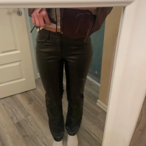 Svarta skinnbyxor - Snygga svarta skinnbyxor med låg midja och bootcut-stil. Byxorna har en knapp och dragkedja framtill samt bälteshällor. Perfekta för en trendig look. Aldrig använda. Jag är ca 172 cm lång och bär storlek S 