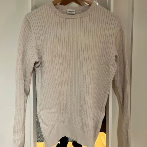 Kabelstickad tröja John Henric - Säljer en stilren beige stickad tröja från John Henric Milano. Tröjan har ett kabelstickat mönster.