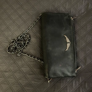 Äkta svart zadig Voltaire väska med kedja - Snygg svart zadigvöska i skinn med kedjedetaljer . Väskan är äkta och köptes för 3000. Observera att den är ganska använd med sminkfläckar (har inte testat att få bort dem) samt missfärgning på silver-örnen. Kanten på väskan är också lite trasig. pris kan diskuteras.