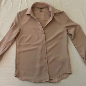 Beige skjorta från H&M - Säljer en stilren beige/rosa skjorta från H&M i storlek XS. Skjortan har långa ärmar och knappar framtill. Perfekt för en elegant look.