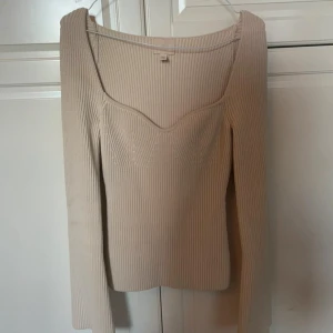 Beige ribbad topp - Säljer en stilren beige ribbad topp med långärmad design och en v-ringad hals. Perfekt för en elegant och avslappnad look. Passar bra till både jeans och kjol.