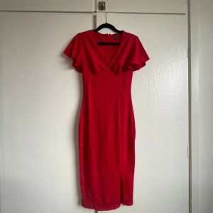 Röd klänning från Shein - Röd klänning från Shein med kortärmade volangärmar och en v-ringning. Klänningen har en slits framtill och en dragkedja bak