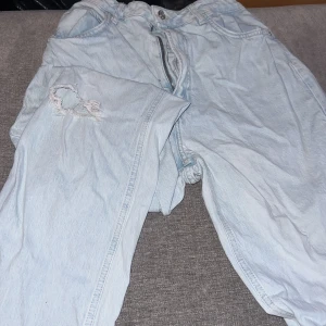 Ljusa jeans med slitning - Säljer ett par ljusa jeans med en cool slitning på ena benet. De har en dragkedja och knapp framtill. Perfekta för en avslappnad stil.