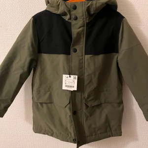 Grön och svart jacka från Zara - Säljer en cool grön och svart jacka från Zara med huva och dragkedja. Jackan har långa ärmar och praktiska fickor framtill. Perfekt för kyligare dagar med sin stilrena design.