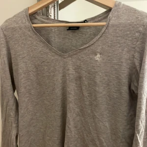 Grå långärmad tröja från Ralph Lauren Sport - Säljer en stilren grå långärmad tröja från Ralph Lauren Sport. Tröjan har en v-ringad hals och är tillverkad i mjukt bomullsmaterial. Perfekt för en avslappnad och bekväm stil.