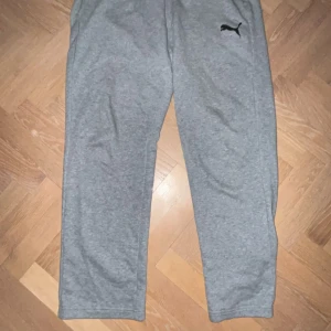 Puma mjukisbyxor - Säljer ett par grå mjukisbyxor från Puma med en klassisk logga på sidan. Byxorna har en avslappnad passform och är perfekta för en bekväm dag hemma eller träning. De är tillverkade i mjukt material för extra komfort.