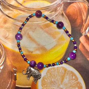 Färgglatt armband med elefantberlock - EGENGJORT armband med lila och turkosa pärlor samt en silverfärgad elefantberlock. Perfekt för att ge en bohemisk touch till din stil.