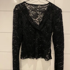 Svart spetsblus från Gina Tricot - Säljer en elegant svart spetsblus från Gina Tricot. Blusen har långa ärmar och ett vackert blommigt mönster. Perfekt för att lägga till en touch av stil till din garderob. Passar bra till både jeans och kjol.