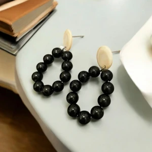 Svarta pärlörhängen med beige detaljer - Snygga örhängen med svarta pärlor i en oval form och beige runda detaljer vid fästet. Perfekta för att ge en elegant touch till din outfit.