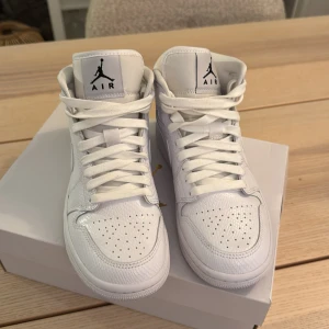 Vita Nike Air Jordans - Säljer ett par stilrena vita Nike Air Jordans med klassisk snörning och hög design. Skorna har perforerade detaljer på tån för extra ventilation och en ikonisk logga på plösen. Perfekta för dig som vill ha en tidlös sneaker i garderoben. Använt två gånger bara.