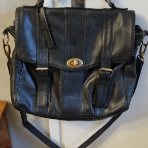 Svart läderportfölj med axelrem  - Svart klassisk läderportfölj med avtagbar axelrem. Väskan har ett vridlås i guld och ett dragkedjefack i mitten. 