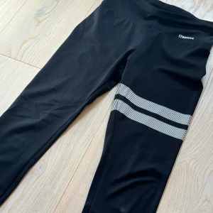 Svarta leggings från Stronger - Säljer ett par svarta leggings från Stronger i storlek S. De är superbekväma och perfekta för träning. Leggingsen har vita diagonala ränder runt ena benet och en praktisk mobilficka. Stretchigt material. Skicket är relativt bra, se tryck på bild 4