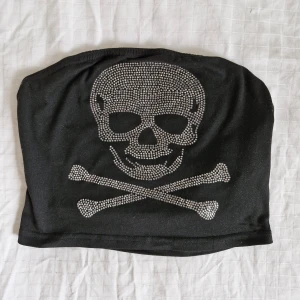 Svart tubtopp med dödskalle från Romwe - Säljer en cool svart tubtopp från Romwe med en glittrig dödskalle på framsidan. Toppen är i storlek S och har ett bekvämt, stretchigt tyg. Perfekt för en festlig kväll eller när du vill ha en edgy look!