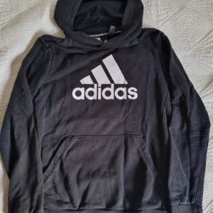 Säljer en svart hoodie från Adidas i storlek L, 164.Den är superbekväm och perfekt för både sport och vardag. Hoodien har en stor vit Adidas-logga på framsidan och en praktisk magficka. Perfekt för höst och vinter! Använd i ok skick.