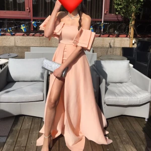 Champagnefärgad långklänning - Säljer en superfin champagnefärgad långklänning med offshoulder-ärmar och volangdetaljer. Perfekt för sommarens fester eller bal! Klänningen har en elegant slits framtill och är i ett lätt och flödande material. Passar perfekt för en glamorös kväll.