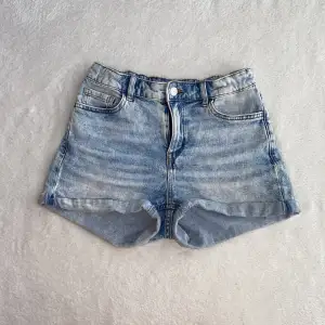 Säljer ett par ljusblå jeansshorts i klassisk stil. De har en normal passform med fem fickor och en knappgylf. Perfekta för sommardagar eller festivaler! 🕶️