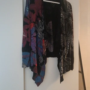 Färgglad mönstrad jacka från Desigual - Säljer en supercool och färgglad kofta från Desigual. Den har ett unikt mönster med blommor och abstrakta former i lila, blått, rött och svart. Koftan är dekorerad med paljetter som ger den en extra glittrig touch. 