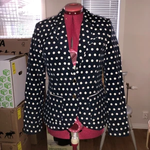 Prickig kavaj - Bra skick. Prickig kavaj med röd insida. Två ytterfickor, innerfickan är dock fejk. Axelvadderad