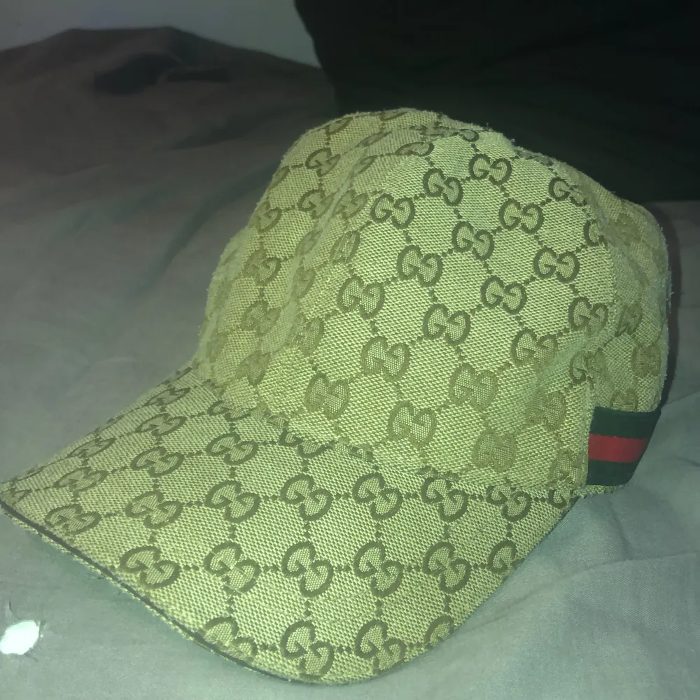 Säljer en snygg beige keps från Gucci med deras ikoniska GG-mönster över hela tyget. Kepsen har en klassisk design med en justerbar rem baktill och en röd och grön randdetalj på sidan. Pris kan sänkas till 500kr vid snabb köp!. Accessoarer.