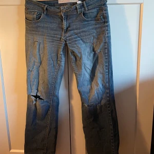 Lågmidjade jeans med slitningar - Säljer ett par blå lågmidjade jeans med slitna detaljer. De har hål som man ser i sista bilden men syns inte mycket när man har på sig de. Väldigt sköna och stretchiga! 